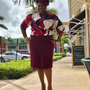 May include: A woman wearing a red, white and black patterned blouse with a burgundy skirt and burgundy heels. She is standing on a pavement in front of a shop with a sign that says "Nature's Remedy, Green Discount, 30 Hours, Blood Analysis".