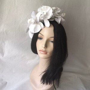 May include: White flower headband with large white orchid blossoms. The headband is made of a white material and is decorated with several white orchid flowers.