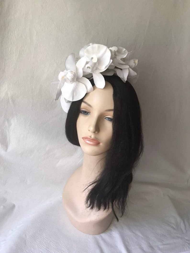 May include: White flower headband with large white orchid blossoms. The headband is made of a white material and is decorated with several white orchid flowers.
