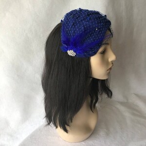 May include: A royal blue velvet and netting hat with a feather and rhinestone embellishment.