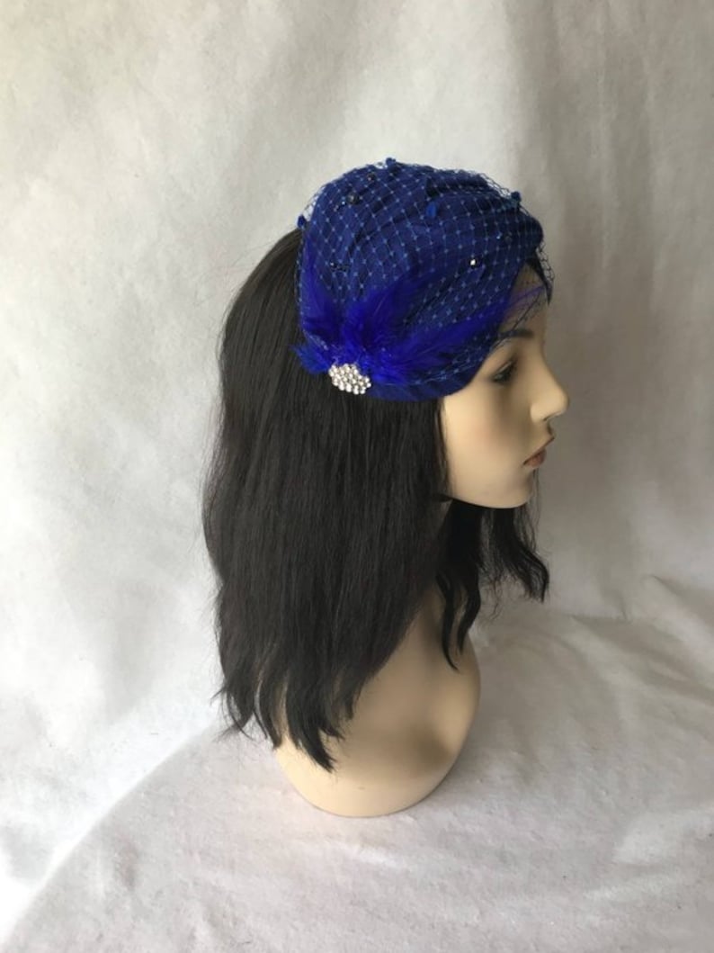 May include: A royal blue velvet and netting hat with a feather and rhinestone embellishment.