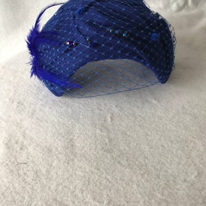 May include: A blue felt hat with a blue veil and blue feather embellishment. The hat is decorated with small, sparkly rhinestones.