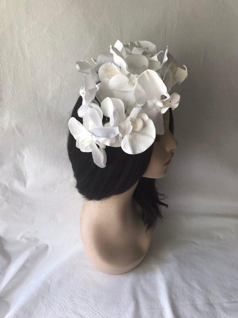 May include: A white flower crown made of artificial orchids. The crown is worn on a mannequin head with black hair.