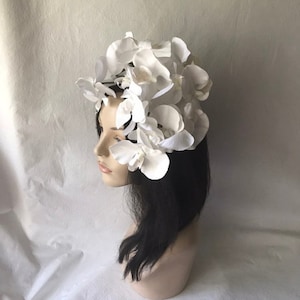 May include: A white flower crown made of artificial orchids. The crown is worn on a mannequin with black hair.