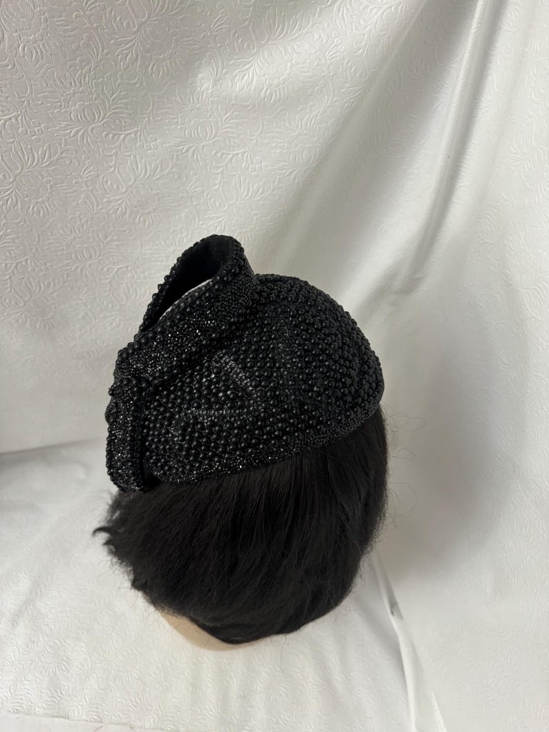 May include: A black beaded hat with a rounded shape. The hat is made of small, black beads that are sewn together.
