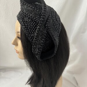 May include: A black beaded headband with a unique, sculptural design. The headband is made of small, black beads that are sewn together to create a three-dimensional shape.