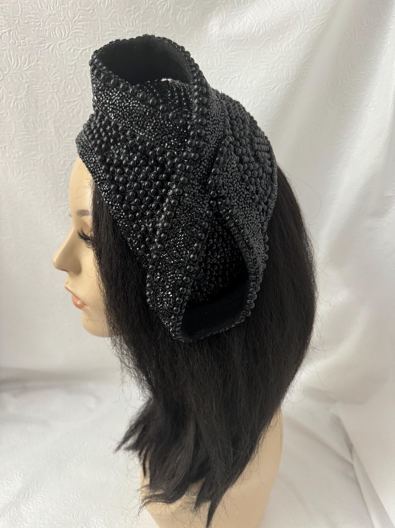 May include: A black beaded headband with a unique, sculptural design. The headband is made of small, black beads that are sewn together to create a three-dimensional shape.
