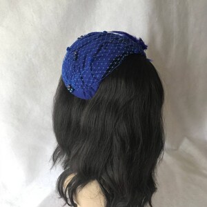 May include: A royal blue velvet pillbox hat with a netting veil and a small feather accent.