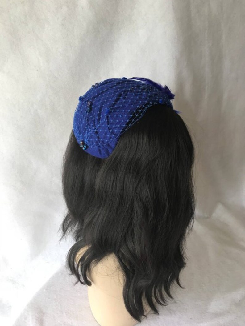 May include: A royal blue velvet pillbox hat with a netting veil and a small feather accent.