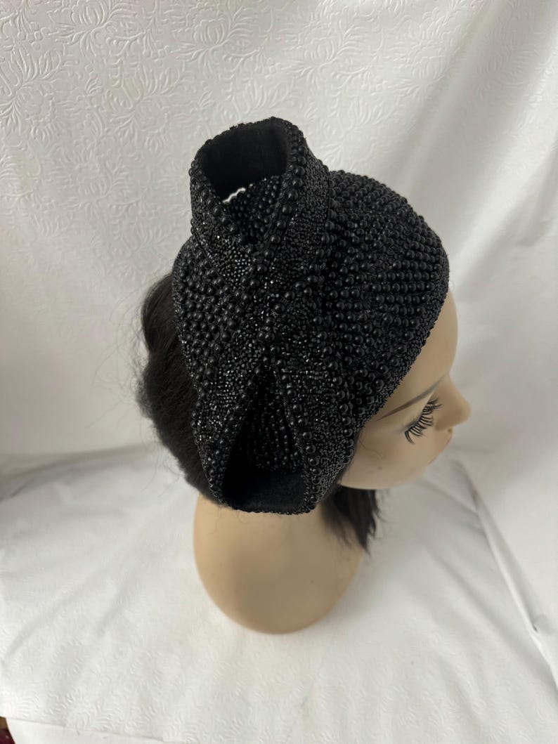 May include: A black beaded headband with a large bow on top. The headband is made of small, round beads that are sewn together.