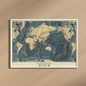 May include: A framed wall map titled The Floor of the Oceans, featuring a detailed bathymetric rendering of the world's underwater topography in shades of deep blue and cream, displayed in a simple white frame against a solid neutral wall.