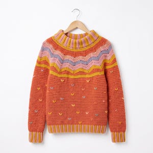 Puede incluir: Un suéter de ganchillo de manga larga con una base de color naranja óxido, cuello y puños acanalados con rayas alternas en rosa y amarillo. El canesú presenta un patrón de chevrón en lavanda, rosa y amarillo, con pequeños detalles bordados.