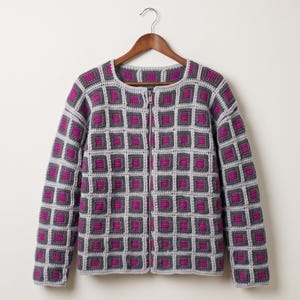 Puede incluir: Una chaqueta de ganchillo de manga larga con un patrón de cuadrados repetitivos en tonos magenta, gris oscuro y gris claro. La prenda tiene un cuello redondo y un cierre de cremallera de metal plateado en la parte delantera central.