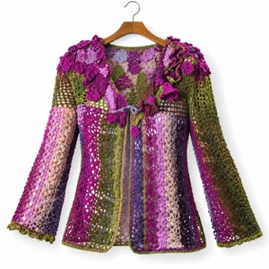 Puede incluir: Un cárdigan de ganchillo de manga larga con una mezcla vibrante de hilos en color morado, magenta y verde oliva. La prenda tiene una abertura frontal con un cierre de lazo, un cuello con flores texturizadas y un complejo patrón calado.