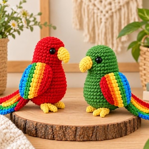 May include: Two handmade crochet parrots, one primarily red and the other green, both featuring yellow beaks and feet. Each bird has wings and a tail crafted with vibrant rainbow-colored yarn stripes, including red, orange, yellow, green, and blue.