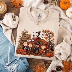 May include: A beige crewneck sweatshirt featuring a graphic of Peanuts characters in Halloween costumes standing in front of a red pickup truck. The print includes pumpkins, autumn leaves, and a wooden sign that reads Happy Halloween.