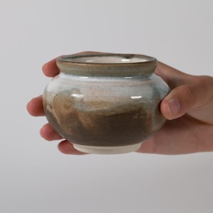 May include: A small, rounded ceramic bowl with a wide rim. The exterior features a gradient glaze transitioning from a dark brown base to a lighter tan middle section, topped with a smooth, glossy white and pale blue finish at the rim.