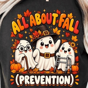May include: A black t-shirt featuring a graphic of three cartoon ghosts surrounded by autumn leaves and pumpkins. The text reads ALL ABOUT FALL (PREVENTION). One ghost wears glasses and holds a cane, another wears a hat, and the third uses a walker.
