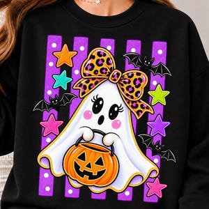 Peut inclure: Un sweat-shirt noir avec un motif de fantôme blanc portant un nœud à imprimé léopard, tenant un seau citrouille orange. Le design comprend des rayures verticales violettes à pois blancs, des étoiles colorées et des chauves-souris noires.