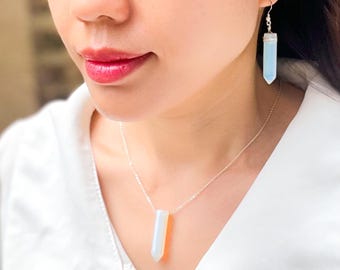 May include: A silver necklace and earrings with a white opal pendant and earrings. The pendant and earrings are shaped like a long, thin, pointed rectangle.