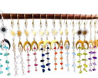 May include: A set of 12 pairs of gold earrings with a sun and crescent moon design. Each pair features a different color of semi-precious gemstone chips hanging from the crescent moon.