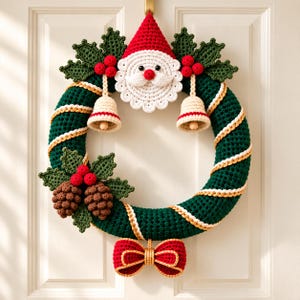 May include: A crocheted Christmas wreath featuring a dark green base with a diagonal gold yarn accent. It is decorated with a central Santa Claus face, two cream-coloured bells, two brown pinecones, green holly leaves, red berries, and a red bow.
