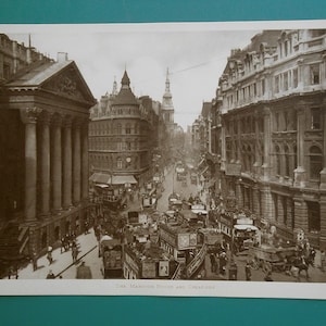 May include: A black and white vintage photograph of a busy street scene in London, England. The photo shows a view of the Mansion House and Cheapside, with horse-drawn carriages and pedestrians in the street.