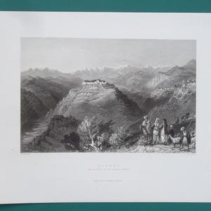 May include: A black and white landscape print depicting a mountainous region with a village atop a hill. Figures in traditional clothing stand in the foreground. The print is on a white background.