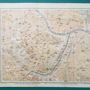 May include: A vintage city map with a grid overlay, featuring streets, buildings, and a river. The map is printed in sepia tones, with detailed text labels. The map is a historical document, likely from the early 20th century.