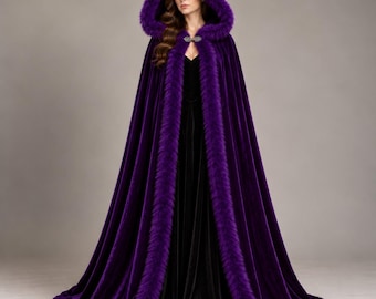 Könnte beinhalten: Ein bodenlanger Umhang aus violettem Samt mit einer tiefen Kapuze und einem dicken, passenden Besatz aus violettem Kunstfell an den Rändern. Das Kleidungsstück wird am Hals mit einer dekorativen silberfarbenen Metallschließe geschlossen.