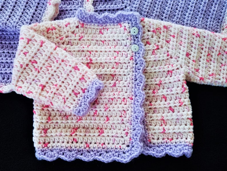 May include: A crocheted baby cardigan with a pink and white color scheme. The cardigan has a scalloped edge and a single button closure.
