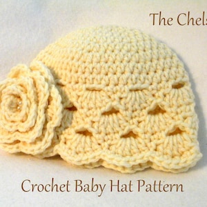 May include: A cream-coloured crocheted baby hat with a decorative flower and scalloped edge. The hat has an openwork design and is labelled "The Chelsey" and "Crochet Baby Hat Pattern". The hat is made of yarn.