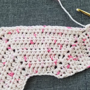 May include: A close-up of a crocheted piece in white and pink yarn. The piece is worked in a circular pattern and has a scalloped edge.