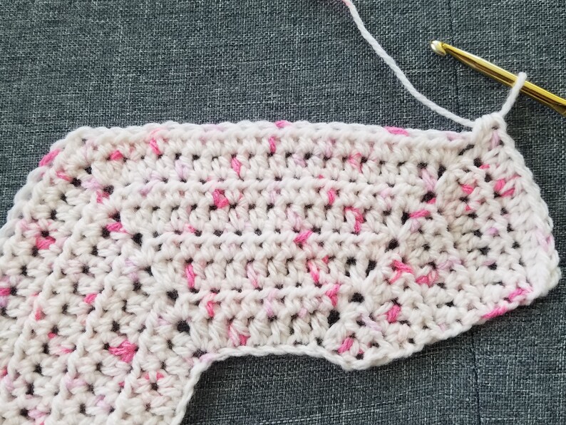 May include: A close-up of a crocheted piece in white and pink yarn. The piece is worked in a circular pattern and has a scalloped edge.