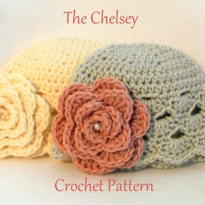 May include: Three crocheted hats in cream, dusty rose, and grey, each adorned with a large, decorative flower. The hats are handmade, with the text "The Chelsey Crochet Pattern" in red.