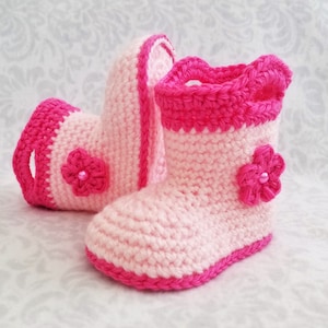 May include: A pair of pink and hot pink crocheted baby booties with a flower embellishment on each bootie.