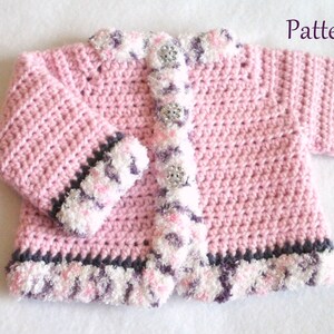 May include: Pink crocheted baby cardigan with a white and purple trim. The cardigan has a button closure and is made with a soft yarn.