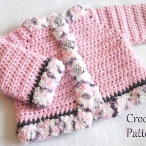 May include: Pink crocheted baby cardigan with a white and purple trim. The cardigan has a button closure and is made with a soft, fluffy yarn.