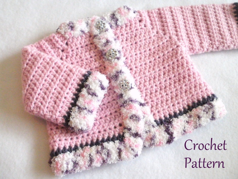 May include: Pink crocheted baby cardigan with a white and purple trim. The cardigan has a button closure and is made with a soft, fluffy yarn.