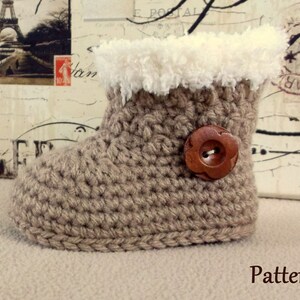 K&ouml;nnte beinhalten: Ein geh&auml;kelter Babyschuh mit einem braunen Knopf und einem wei&szlig;en Kunstfellbesatz. Der Schuh ist beige und hat eine geh&auml;kelte Sohle. Muster.