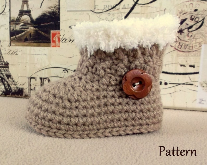 K&ouml;nnte beinhalten: Ein geh&auml;kelter Babyschuh mit einem braunen Knopf und einem wei&szlig;en Kunstfellbesatz. Der Schuh ist beige und hat eine geh&auml;kelte Sohle. Muster.