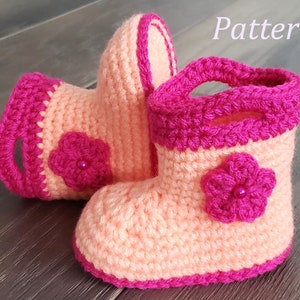 May include: A pair of crocheted baby booties in peach and pink with a flower detail. The booties have a pink trim and a pink flower with a pearl bead in the center.