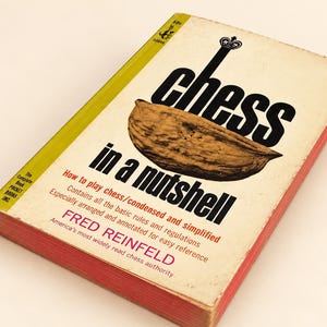 May include: A paperback book titled Chess in a Nutshell by Fred Reinfeld. The cover features a large brown walnut graphic, black text, and red accents. The spine is yellow, and the page edges are stained red. It is a Pocket Books edition.
