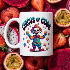 May include: A white ceramic mug featuring a colourful illustration of a clown with red hair, wearing a blue and yellow outfit, holding orange cubes. The text Circus of Code is printed above the clown in a dark blue, arched font style.