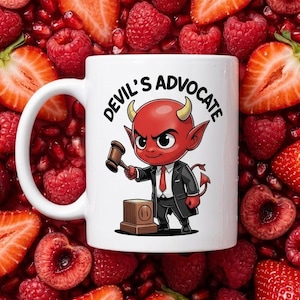 May include: A white ceramic mug featuring a cartoon illustration of a red devil character in a black suit and red tie, holding a wooden gavel. The text "DEVIL'S ADVOCATE" is printed in black above the character, who stands next to a wooden block.