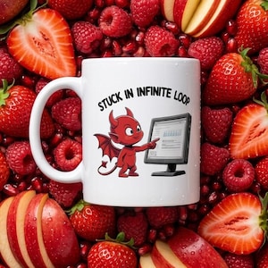 May include: A white ceramic mug featuring a cartoon red devil pointing at a computer monitor with the text STUCK IN INFINITE LOOP printed above the character. The mug is surrounded by a dense arrangement of fresh strawberries, raspberries, and apple slices.