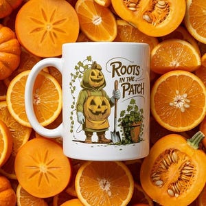 May include: A white ceramic mug featuring a graphic of a pumpkin-headed character wearing a green hooded sweatshirt and apron, holding a shovel next to a potted plant, with the text Roots in the Patch printed in a dark brown script font.