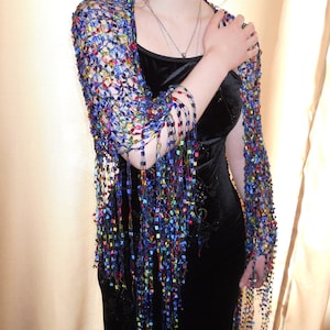 May include: A blue and multi-colored beaded shawl with fringe. The shawl is draped over a person wearing a black dress.