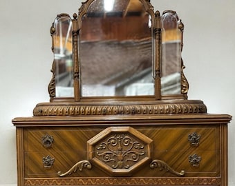 May include: An antique wooden dresser with a tri-fold mirror. The dresser features ornate carvings, decorative hardware, and a warm brown finish. The mirror is framed with detailed molding. The text "Laura Designs Shop" is visible at the bottom.