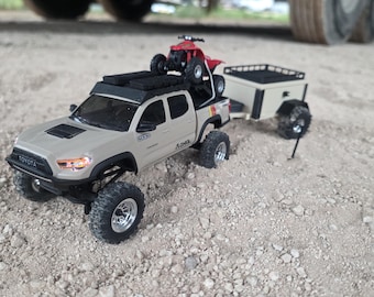 Puede incluir: Un modelo de camioneta Toyota beige con molduras negras, una baca que transporta un pequeño quad rojo y un remolque utilitario beige a juego enganchado en la parte trasera. El vehículo cuenta con neumáticos todoterreno y llantas plateadas.